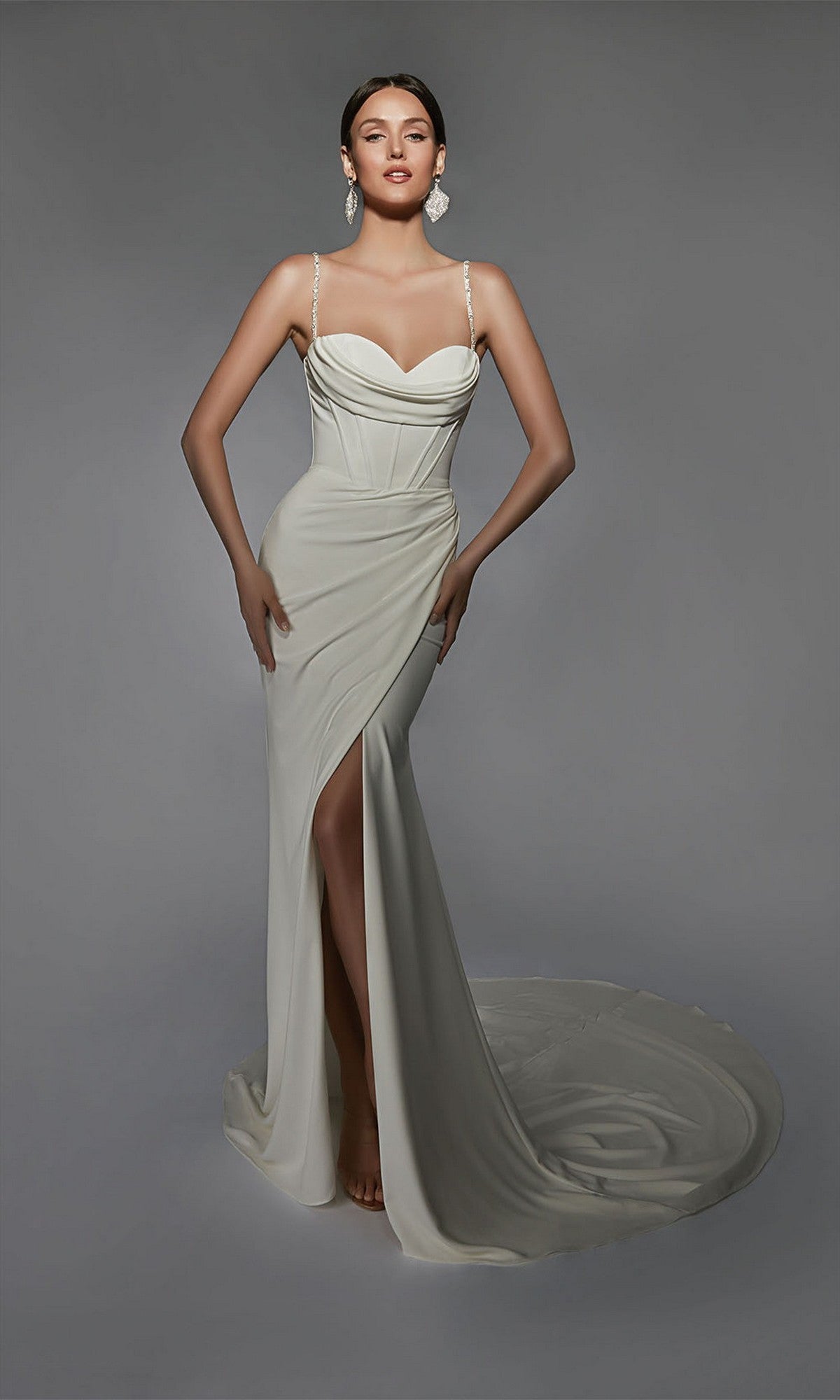 A woman models the Alyce 7103 long white dress, featuring a fitted stretch design with a sweetheart neckline, thin straps, corset bodice, and thigh-high slit. She stands against a plain gray background.